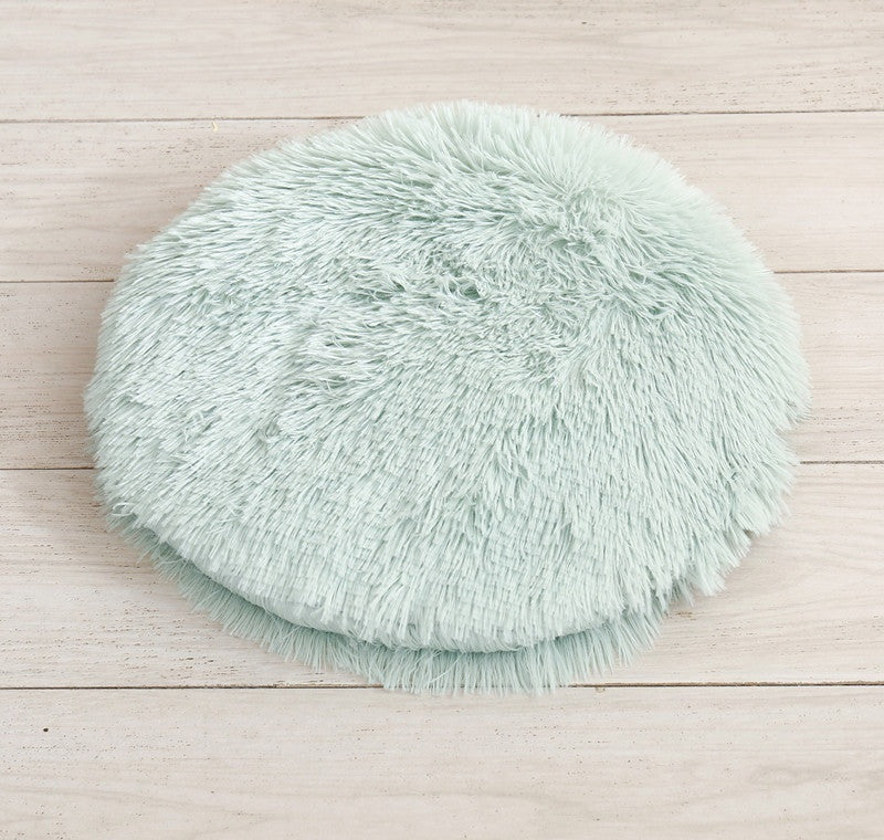 Round long-pile plush cat cushion in mint green on a white table