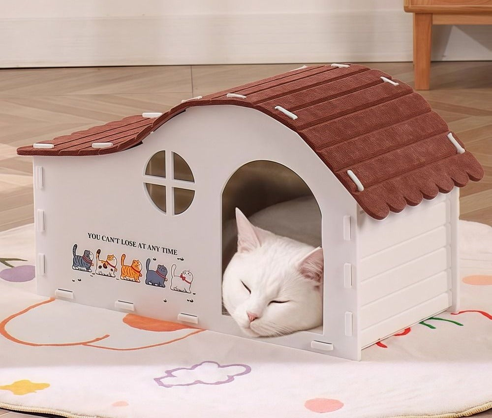 White cat resting in the doorway of the white felt cat house with a red roof