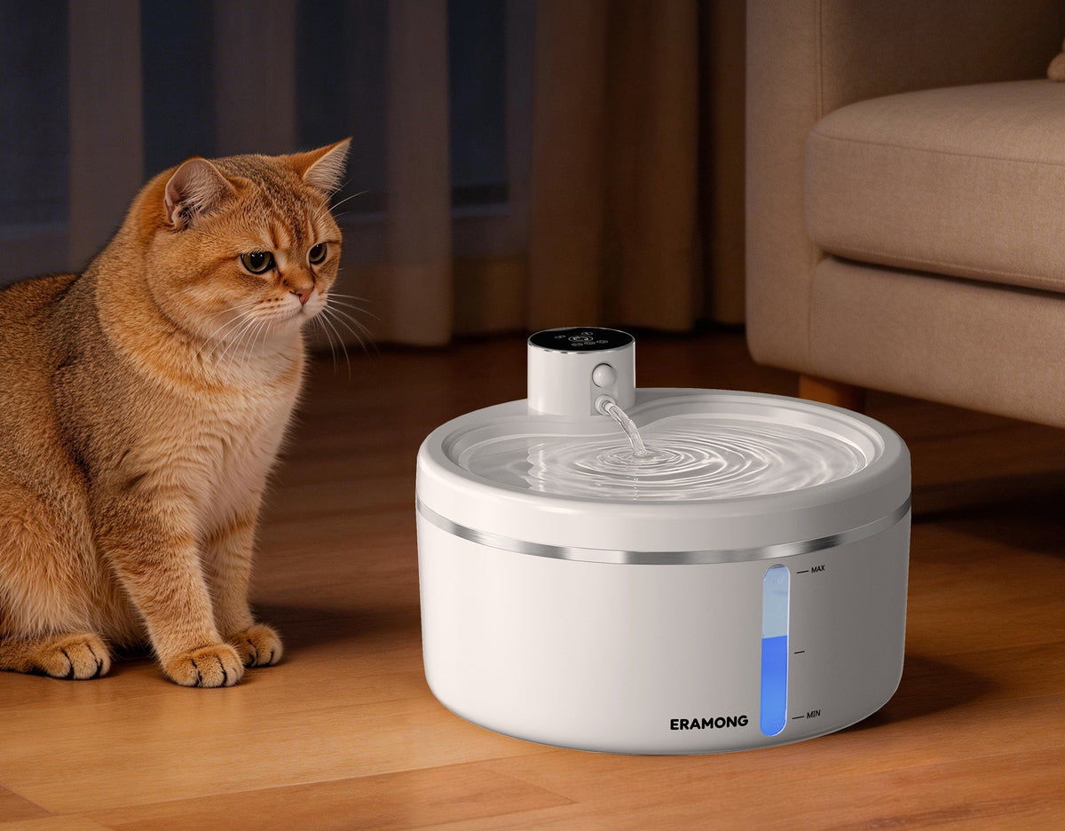 An orange cat sits beside the white ERAMONG water fountain near a sofa