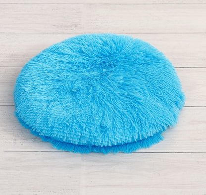 Round long-pile plush cat cushion in bright blue on a white table