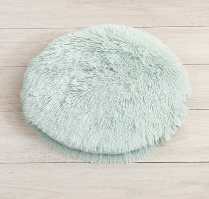 Round long-pile plush cat cushion in mint green on a white table