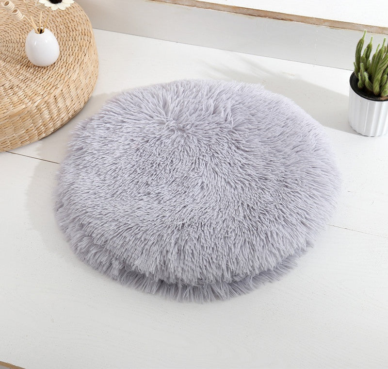 Round long-pile plush cat cushion in light grey on a white table