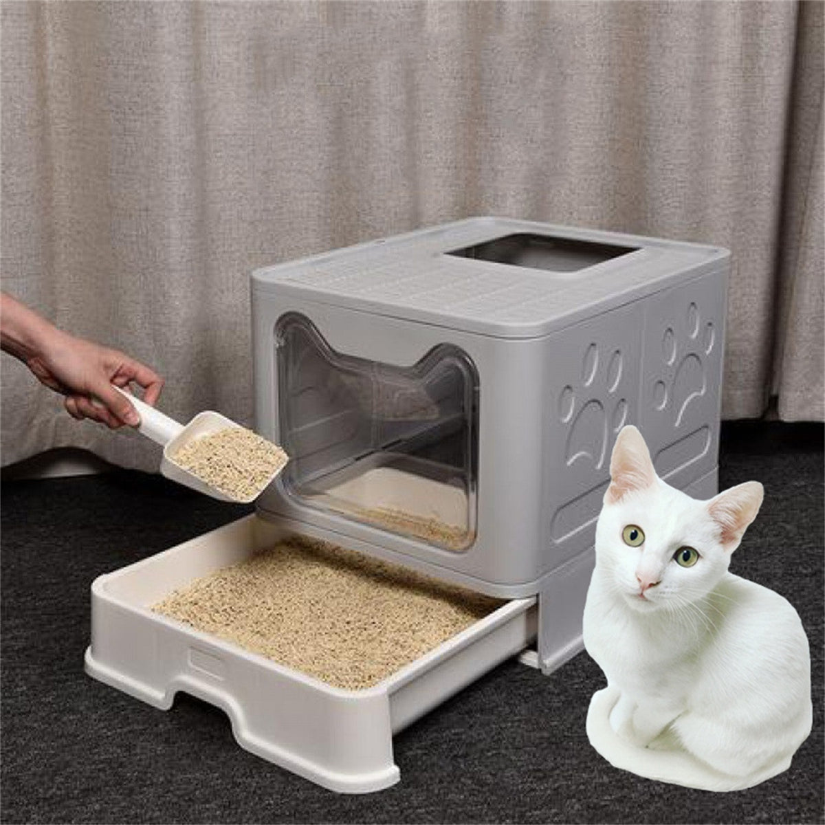 Hand scooping litter from the pulled-out drawer of the grey litter box, a white cat beside it