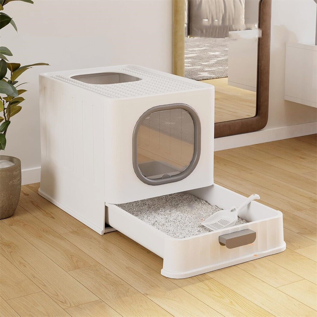 White enclosed litter box with the drawer pulled out, litter and a scoop inside, on a wooden floor