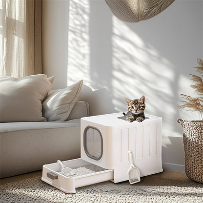 Kitten peeking out of the top of the white litter box in a living room, drawer open with litter and a scoop