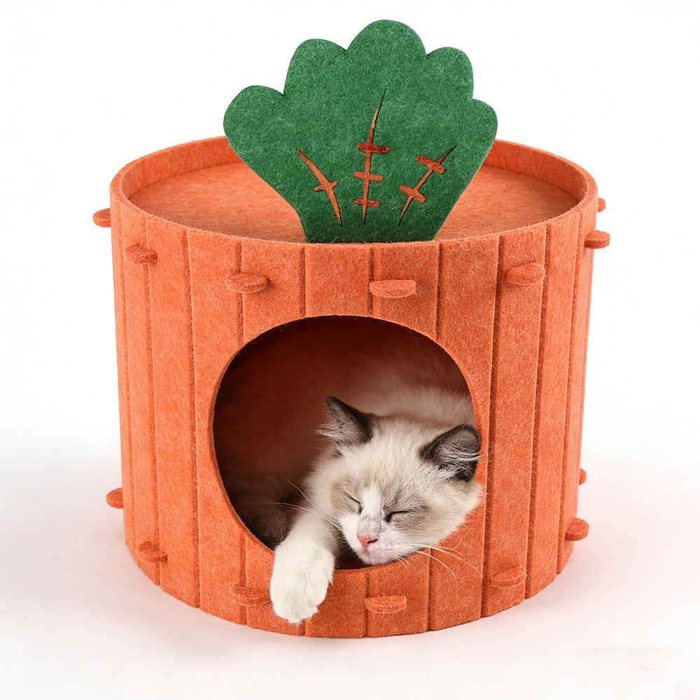 A cream cat with dark ears sleeps inside the orange felt carrot cave, one paw on the round entrance