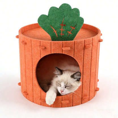 A cream cat with dark ears sleeps inside the orange felt carrot cave, one paw on the round entrance