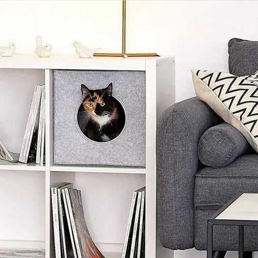 Light grey felt cube cat cave in a shelf, a calico cat looking out of its round opening