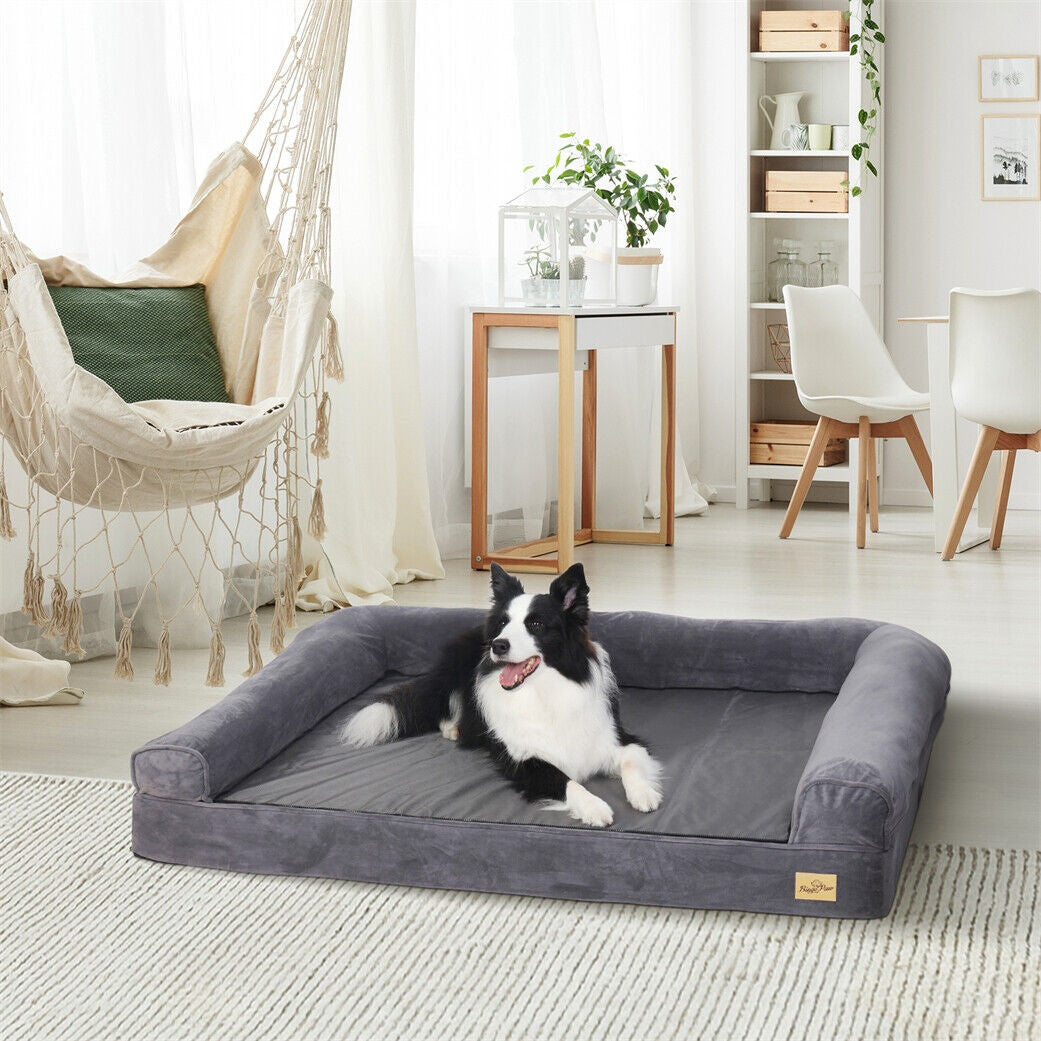 Grey dog sofa bed with bolsters on three sides and an open front, shown with its zip-on plush top removed, a border collie lying on it