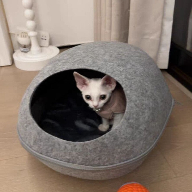 A white kitten looking out of the front opening of the grey felt pod