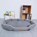 Grey oval bolster dog bed with cream piping and a tufted cushion on a grey rug, small sewn label on the front