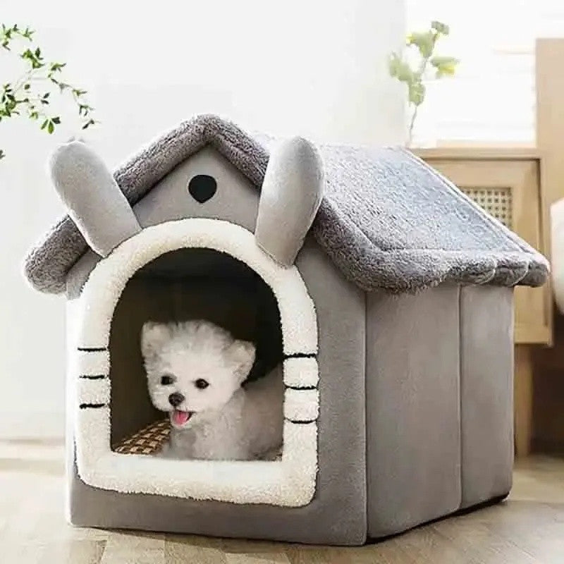 Grey plush pet house with a gabled roof, two ears and a cream-trimmed doorway, a small white dog inside