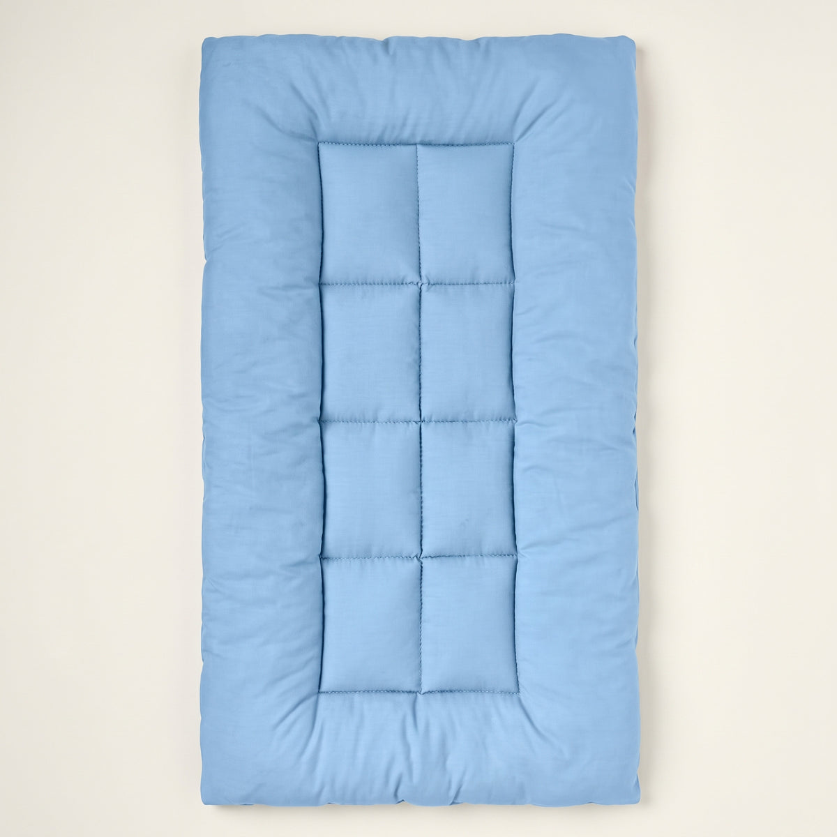 Light-blue quilted rectangular pet mat seen from above on a warm off-white backdrop