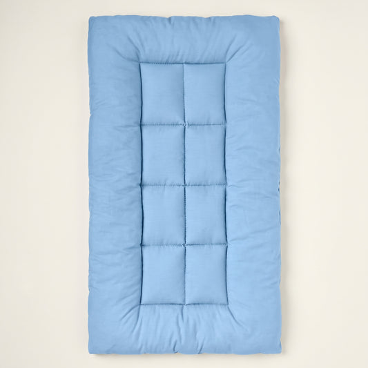 Light-blue quilted rectangular pet mat seen from above on a warm off-white backdrop