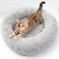 A tabby kitten stretches in a grey long-pile donut bed on a white background