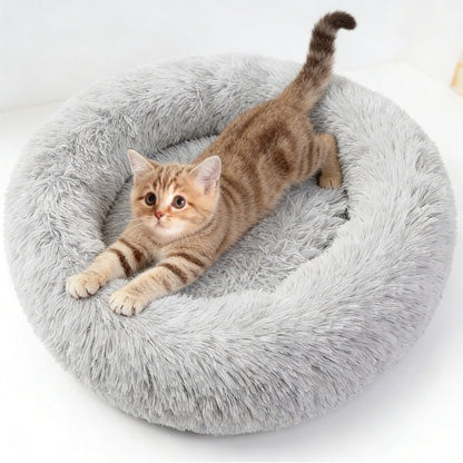 A tabby kitten stretches in a grey long-pile donut bed on a white background