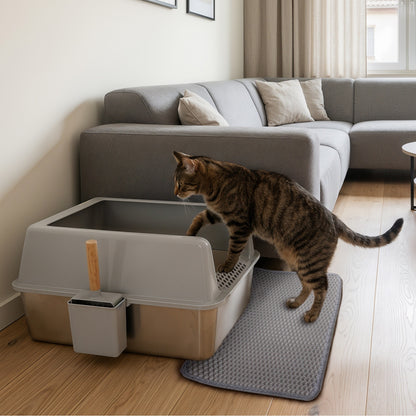 Tabby cat stepping into the grey and silver litter box beside a sofa, with a grey mat underneath